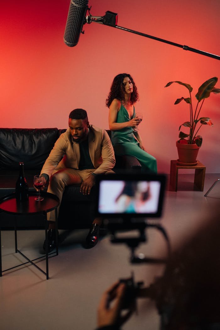 Actors on set with a microphone and video camera during filming, featuring a stylish indoor setting.